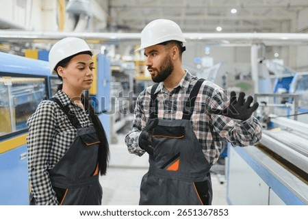 Supervisor wearing hardhat and gloves explaining production process to female worker in modern factory