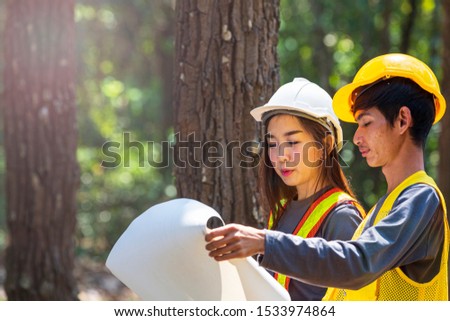 The supervisors are constructing roads in the forest. Young Engineer female holding blueprint on hand. Engineer team working on project at the forest. Technical operaters and Labourers.
