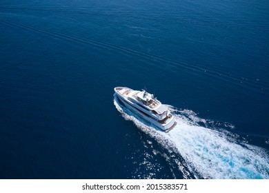 Superyacht is moving fast on the water top view. Motor Yacht in motion top view. A huge super Mega yacht in white on dark blue water in Italy. White yacht on the sea aerial view.