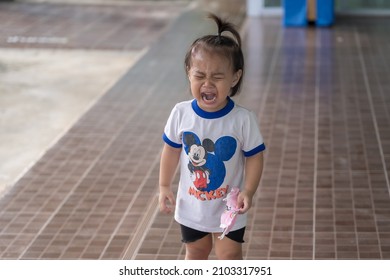 Suphan Buri, Thailand - January 6, 2022: Little Child Girl Crying And Doesn't Want To Wear A Medical Face Mask To Protect Against The Spread Of Covid-19 And Playing Outside With Security Measures. 