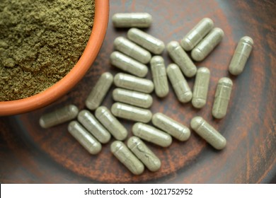 Supplement kratom green capsules and powder on brown plate. Herbal product alt-medicine kratom is  opioid. Home alternative pain remedy, opioid addiction, dangerous painkiller. Selective focus - Shutterstock ID 1021752952