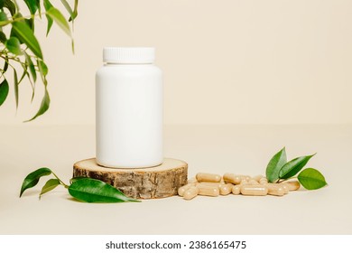Supplement white bottle with herbal pills on wooden podium. Vitamins  bottle mockup with pills and green leaves on beige background, organic medication. Natural herbal vitamins, healthy lifestyle.