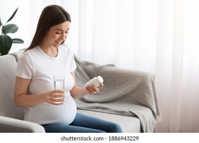 Supplements During Pregnancy. Smiling Pregnant Woman Holding Plastic Jar With Vitamins And Glass With Water, Sitting On Couch At Home, Taking Prenatal Pills For Immunity And Health, Copy Space - Powered by Shutterstock