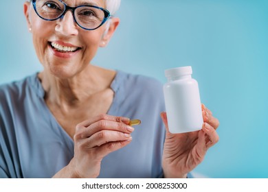 Supplements. Senior Woman Holding Capsule And A Blank White Supplement Container.