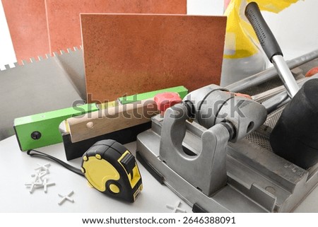 Supply of tools and tiling material on white table and tiled wall. Elevated view.