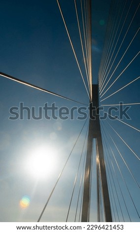 Support and cables of the suspension bridge against the background of the blue sky and the glare of the sunbeam. Buildings and structures in Norway. Vertical photo, bottom view