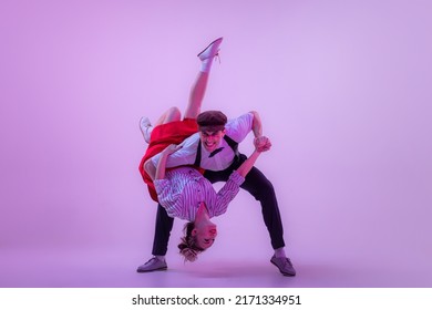 Support. Emotional expressive young man and pretty woman in vintage style outfits dancing retro dance isolated on very peri color background in neon light. American traditions, 1960s fashion and art
