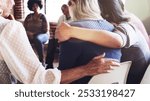 Support group meeting with diverse individuals sitting in a circle hugging and supporting one another. People offering comfort and empathy, showing support and connection in a community setting.