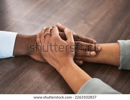 Support, help and couple holding hands for trust, empathy and unity in crisis, cancer or bad news. Solidarity, care and man and woman together on table for praying, comfort and prayer, hope or love.