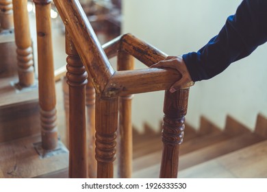 support, help and people concept- Close up of a man's hand holding to a wooden railing while climbing a staircase.