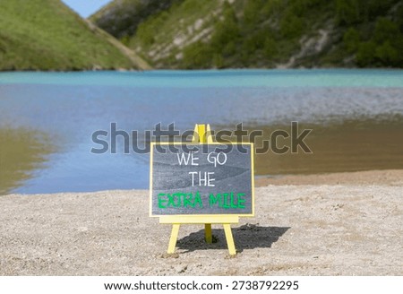 Support, help we go the extra mile symbol. Concept words We go the extra mile on beautiful blackboard. Beautiful mountain lake background. Business we go the extra mile concept. Copy space.