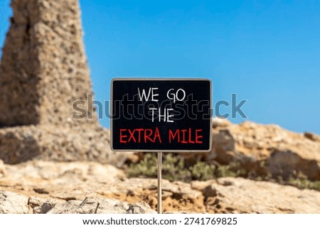 Support, help we go the extra mile symbol. Concept words We go the extra mile on beautiful blackboard. Beautiful stone and blue sky background. Business we go the extra mile concept. Copy space.