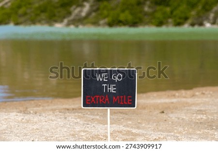 Support, help we go the extra mile symbol. Concept words We go the extra mile on beautiful blackboard. Beautiful mountain lake background. Business we go the extra mile concept. Copy space.