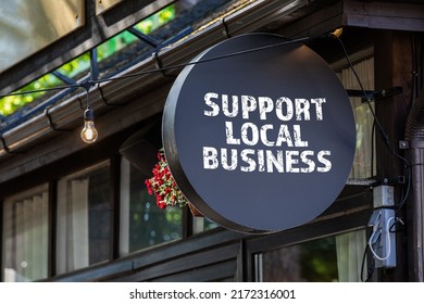 Support local business. Round, black sign onn teh wall of the house.