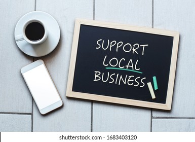 Support Local Business text written on blackboard. Chalk board with coffee and mobile phone.