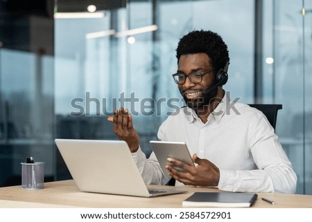 Support service worker at workplace with headset phone and tablet computer in hands. Man consults customers remotely using video call. Business meeting conference remotely.