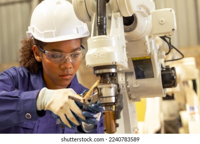 Supporting Engineer african american woman testing an Artificial Intelligent welding robotic automatic arm machine in modern factory. Automation manufacturing for industry 4.0 Technology.  - Powered by Shutterstock