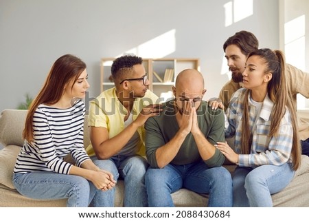 Supporting group of people comfort their sad male friend who shares his problems with friends. Sympathetic friends sit on sofa and say kind words to man. Friendship and support concept