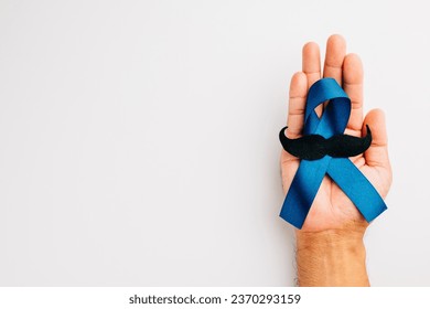 Supporting men's health and Prostate cancer awareness in November. Man's hands hold a light blue ribbon with a mustache on a blue background a symbol of strength and solidarity. - Powered by Shutterstock