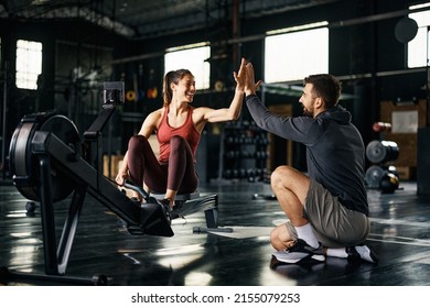 Supportive fitness instructor giving high-five to athletic woman after exercising on rowing machine during cross training in a gym.  - Shutterstock ID 2155079253