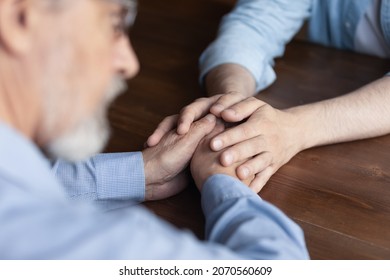 Supportive Hands. Close Up Caring Young Man Adult Child Caregiver Sit At Table Facing Old Man Retiree Support Comfort Express Empathy. Geriatric Psychologist Talk To Elder Patient On Therapy Session