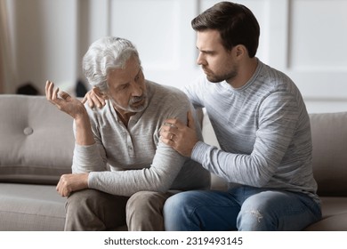 Supportive millennial Caucasian man comfort caress upset elderly 70s father feeling distressed and lonely at home. Caring adult grownup son make peace reconcile with mature dad after family fight. - Powered by Shutterstock