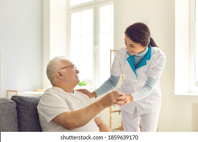 Supportive nurse giving glass of water to happy senior man sitting on couch in nursing home or assisted living facility. Friendly doctor visiting male patient at home and helping him take medicine