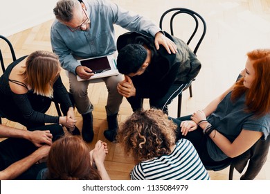 Supportive Therapist Comforting A Young Man Who Lost His Parents In Group Therapy For People In Mourning