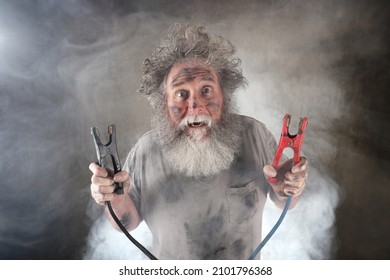 Suprised old man with beard holding jumper cables surrounded by smoke  - Shutterstock ID 2101796368