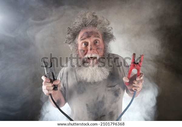 Suprised old man with beard holding jumper cables\
surrounded by smoke 