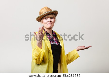 Suprised, shocked woman gardener in sun hat and yellow raincoat waiting for rain, gesturing with hands making funny face
