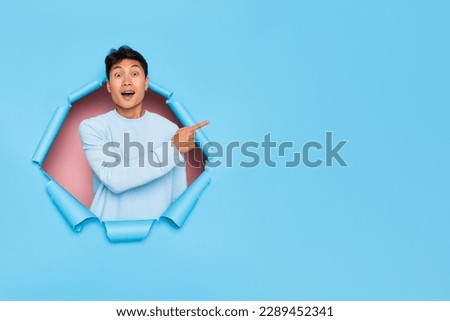 Suprised young man posing in cut on blue studio background, pointing forefinger aside at empty place, shopping time concept, copy space, high quality photo