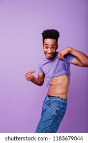 Suprised Young Man Taking Off His T-shirt. Indoor Photo Of Emotional African Model Having Fun During Photoshoot.