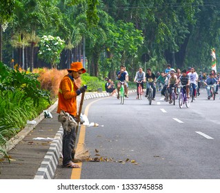 SURABAYA, INDONESIA - MAY 20, 2012: As an award winning clean and green city, Surabaya city's janitor clean the street thoroughly while people are riding their bikes to reduce pollution in Jalan Darmo