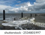 Surf at the dolphins of the old ferry dock in Eckwarderhörne during high tide on a sunny summer