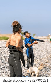 Surf instructor helping student preparing wetsuit before entering the ocean for a surfing lesson on a sunny day