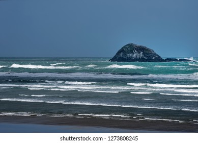 Surf on an empty beach on a windy day under clear skies and a rocky island in the background