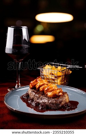 surf and turf close-up with thick slice of sirloin steak and prawns with blackberry jam with red wine in a pub