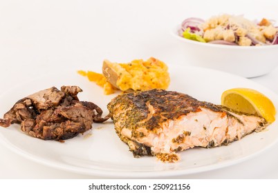 Surf And Turf Dinner - Grilled Wild Salmon On White Plate With Sliced Tenderloin Steak And Twice Baked Potato.  Salad In Background.  Brightly Lit With Copy Space.