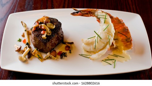 Surf And Turf. Lobster And Steak Entree. Filet Mignon Topped With Chanterelle Mushrooms And Maine Lobster Tail Topped With Drawn Butter Served On White Dinner Plate. Classic Steakhouse Menu Favorite.