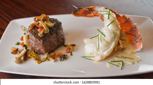 Surf And Turf. Lobster And Steak Entree. Filet Mignon Topped With Chanterelle Mushrooms And Maine Lobster Tail Topped With Drawn Butter Served On White Dinner Plate. Classic Steakhouse Menu Favorite.