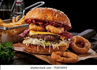 Surf and turf seafood and meat burger with fried squid rings, melted cheese, crispy bacon and a beef patty served on a wooden board with side potato chips - Powered by Shutterstock