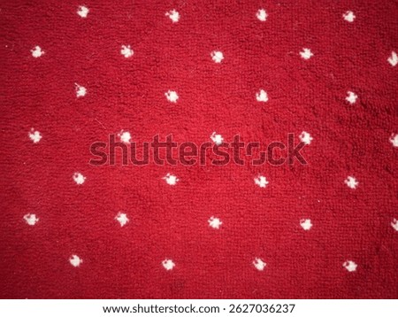 The surface of a dark red carpet with small white dot patterns evenly distributed
