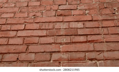 The surface features a classic red brick wall with noticeable wear and tear. The varying shades highlight the texture and rustic appeal of the aged bricks resulting from time and weather.