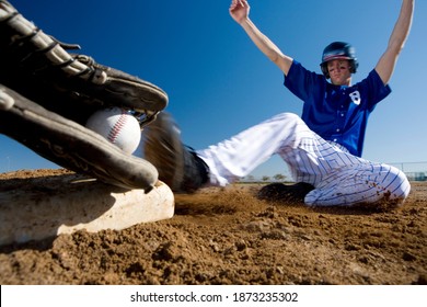 Surface level blurred motion image of a baseball player in blue uniform sliding into a base on the pitch during a competitive game with opposing the player holding the ball.