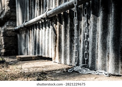 Surface level view of a long metal chain and combination lock attached to a metal pole on a building in the UK. Used to chain up bikes to prevent theft, common in this area.