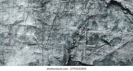 The surface texture of old, worn, and damaged plastic tarpaulin. The surface of the material shows signs of severe weathering, with the outer layer cracked, peeling, and discolored.