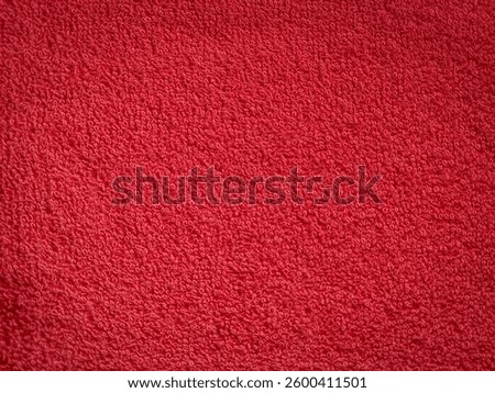 The surface texture of the red bath towel is wavy and wrinkled. The texture of the towel material is made of soft and smooth textile. Top view of a terry cloth bath towel.