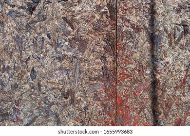 The Surface Of Two Sheets Of Waferboard Which Has Been Painted Red In Places Forming An Exterior Wall.