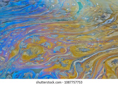 Surface water of a Texas bayou with ripples, showing a colorful oily film on top, signifying polluted oily waters.